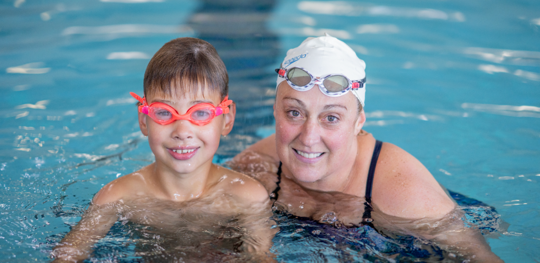 Mother and son smile for the camera in a lap lane while getting in some free swim time in the indoor lap pool at the MCC.