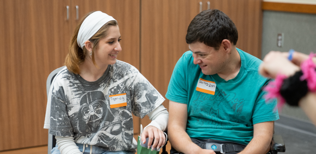 Adaptive participant and their caregiver smile and laugh during an Alice in Wonderland themed adaptive activity.