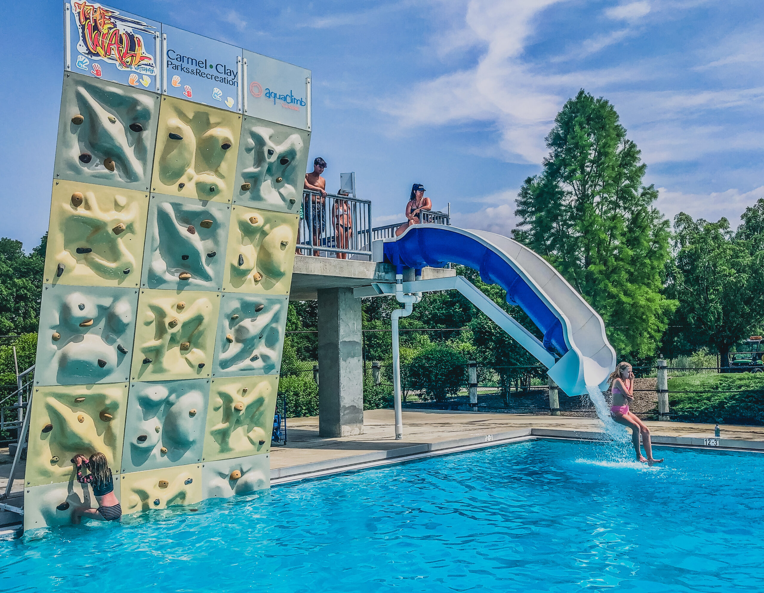 kiddo scales the wall in the dive well at The Waterpark while another splashes into the pool off of the Plunge Slide