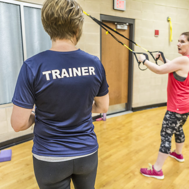 Personal trainer whose back is turned in the foreground works with woman using stretch bands during a session at the MCC.