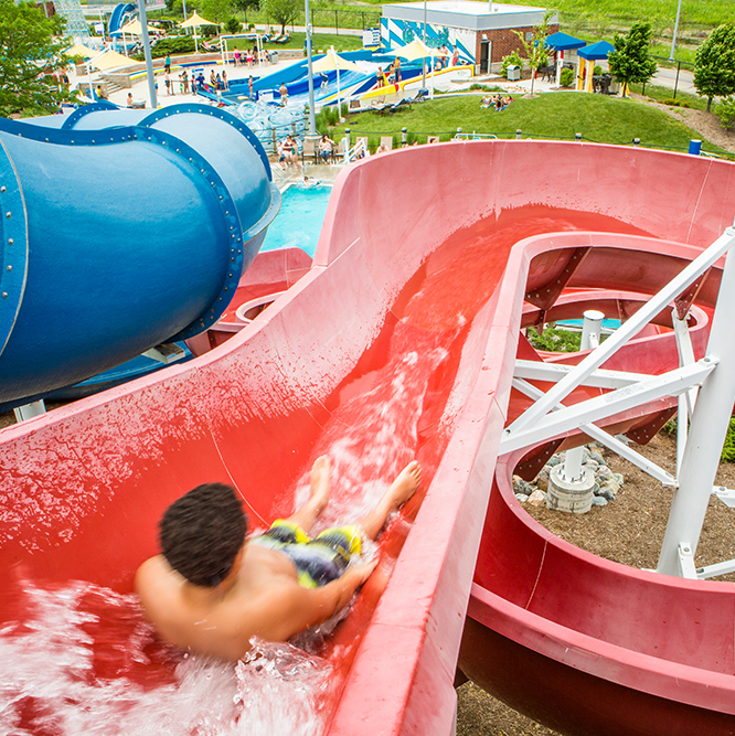 Boy sliding down a red water slide.