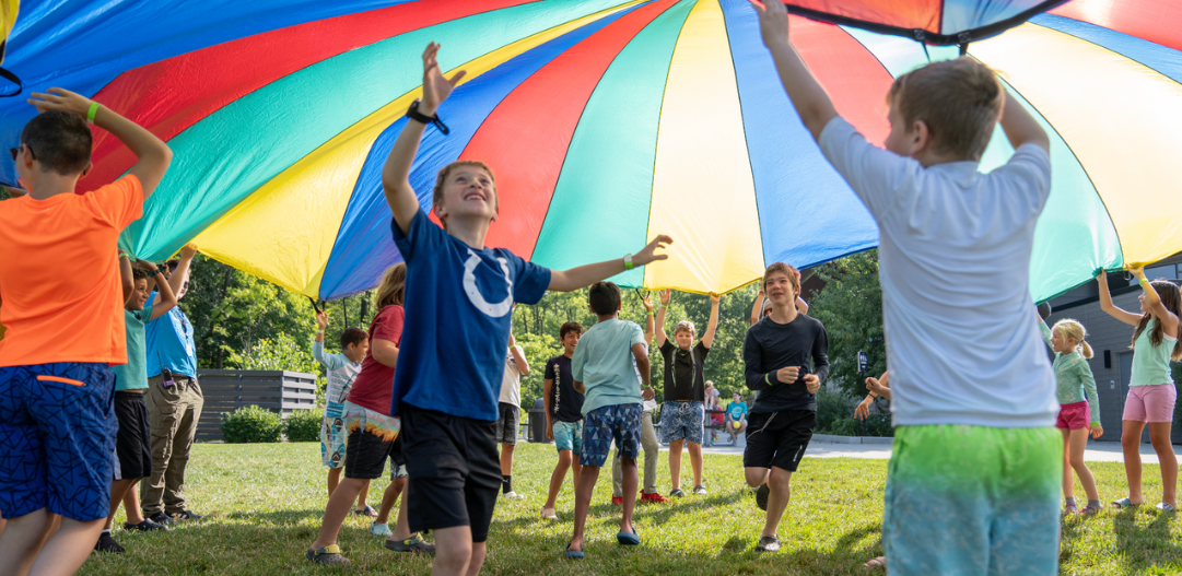 Campers play under a colorful parachute