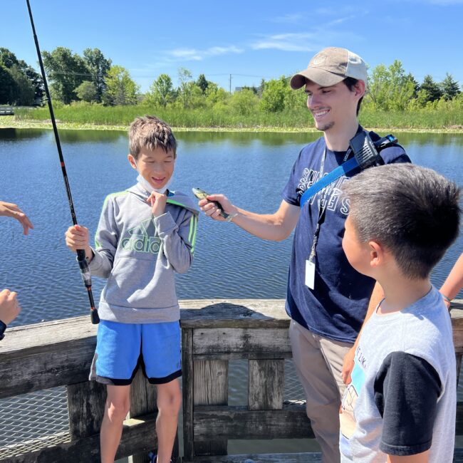 Participants look as a leader holds up the fish they caught off the dock.