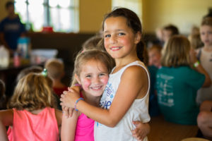Girls hugging and smiling at a summer camp