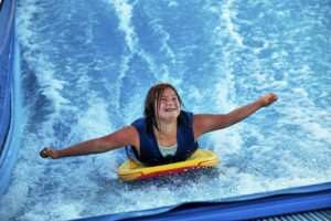 Girl smiling on a surfboard while on the FlowRider in our adaptive program