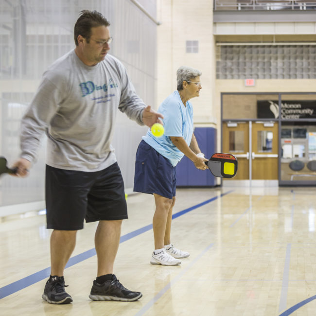 Adult pickleball league players hit the ball across the net in the MCC gymnasium.