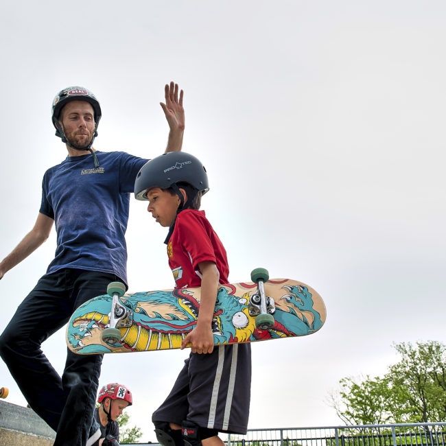 Young skateboarder gets a high five from skate park coach.