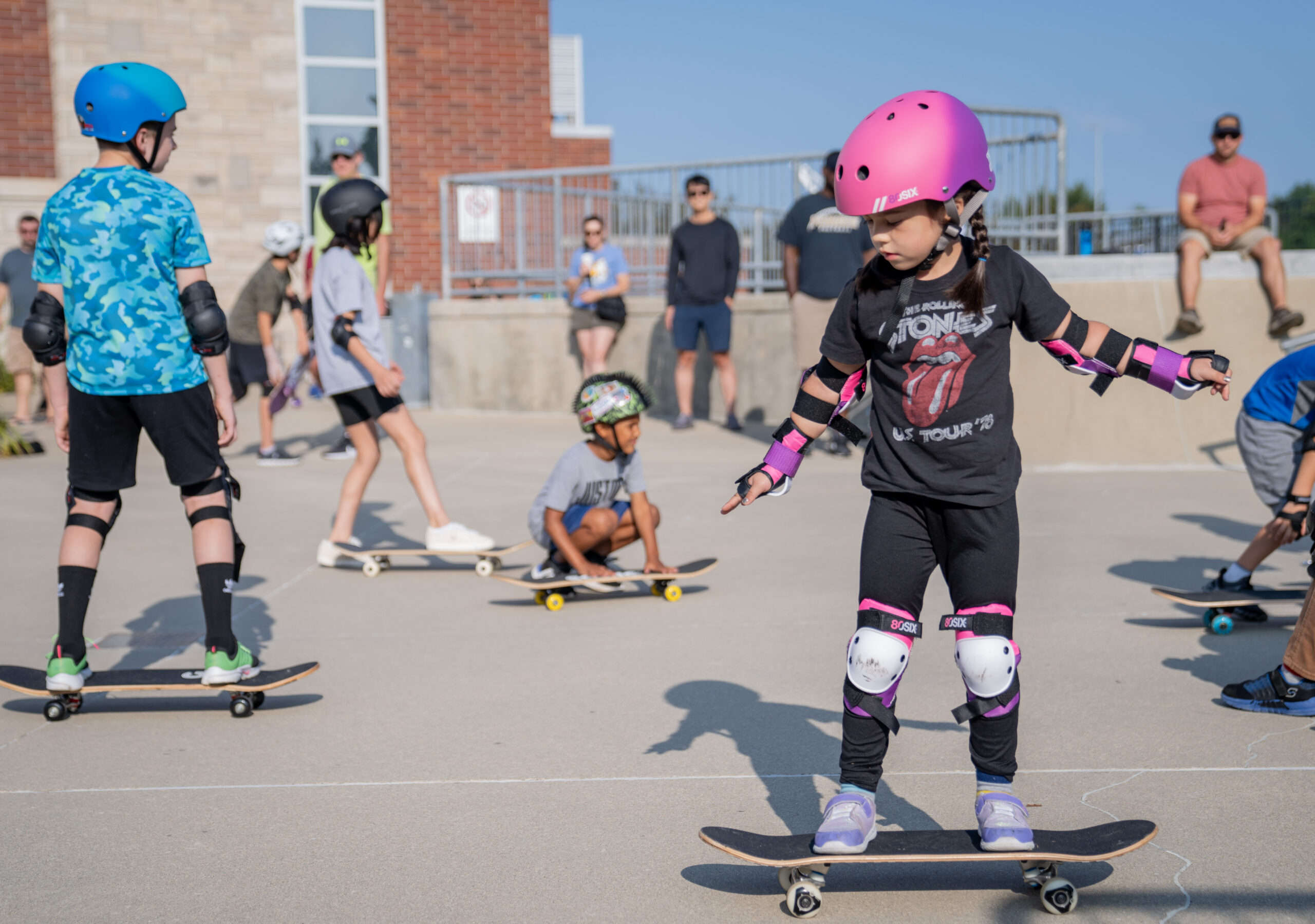 Girl learns how to stay on her skateboard out at the Skatepark during a beginner class.