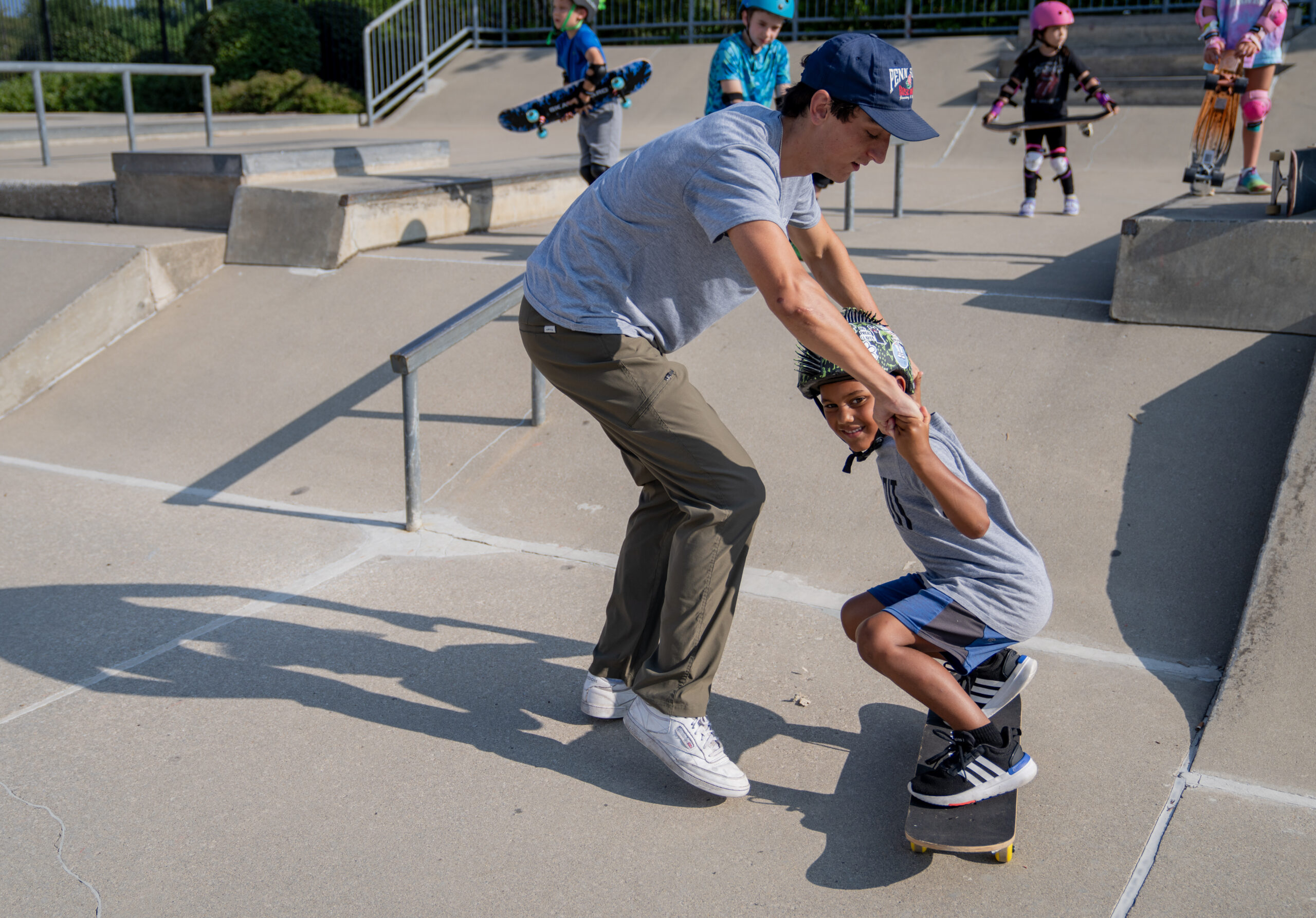 Skateboarding instructor works with beginner student at Skatepark on standing up on the board.