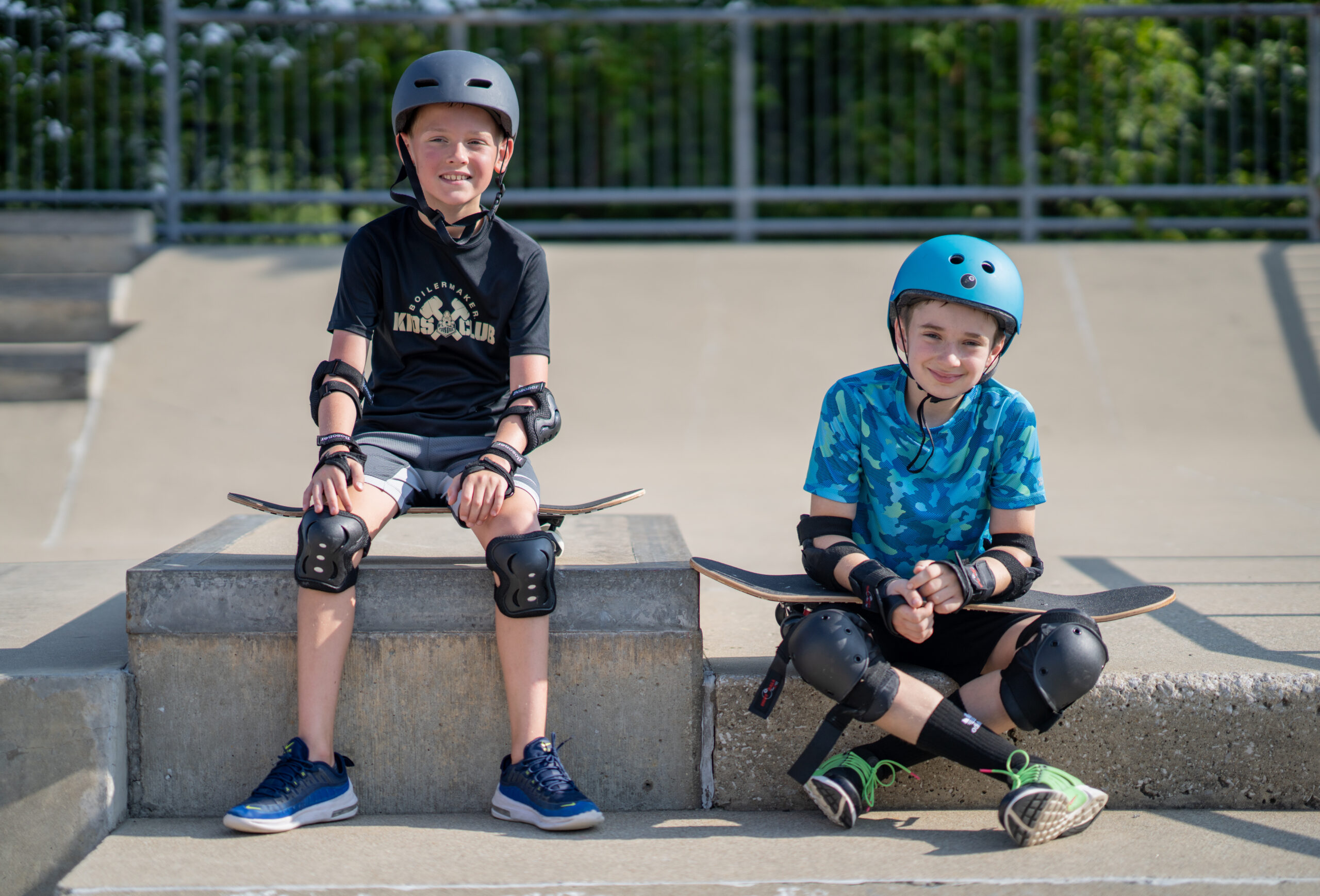 Two beginner skateboard students smile at the camera out at the Skatepark.