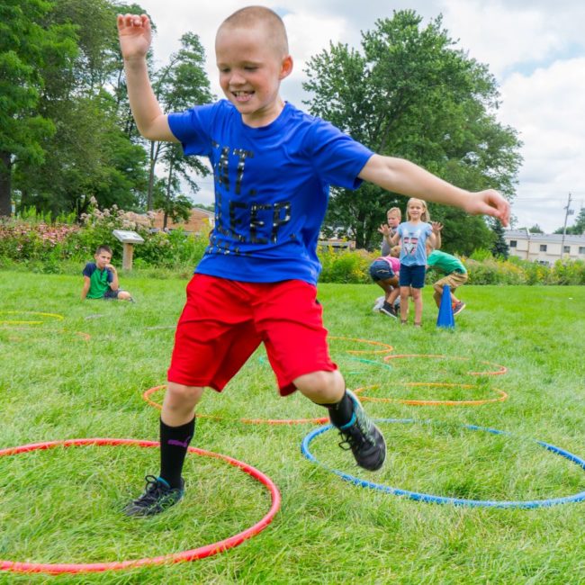 Child in a summer camp jumping through hula hoops as part of a game.
