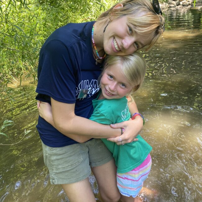 Counselor hugs participant in the river while exploring at Camp Wayback.