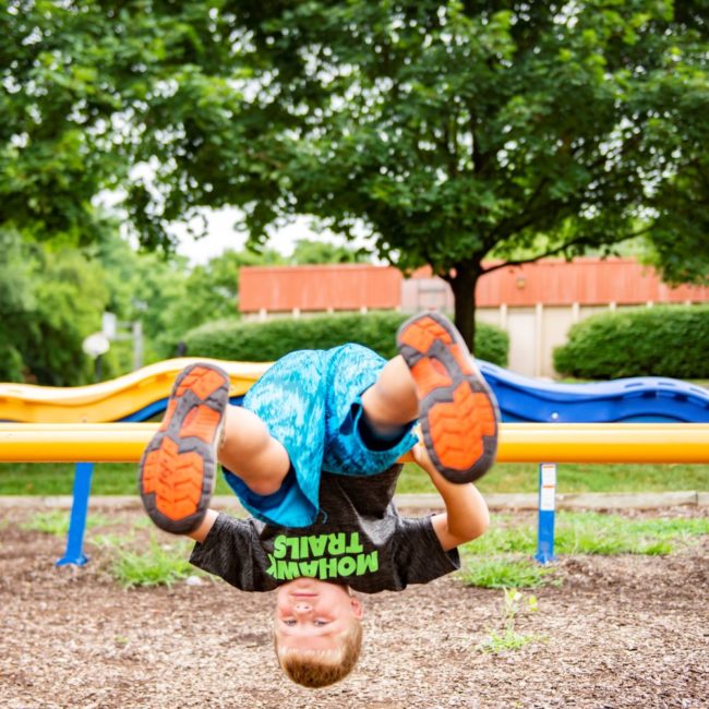 Kid in summer camp upside down on playground equipment.