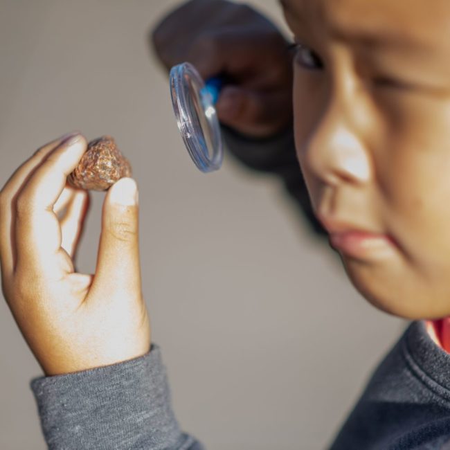 Boy looking at a rock up close with magnifying glass