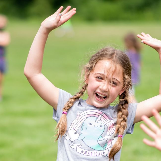 Girl in a summer camp with joyful hands in the air