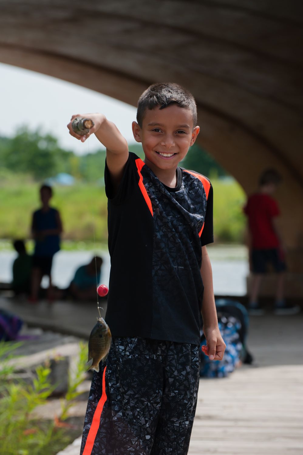 Boy in a summer camp holding up fish he caught on his homemade fishing rod.
