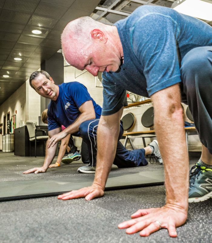 Personal trainer works with adult client on stretching with one leg forward in the MCC fitness center on the floor.