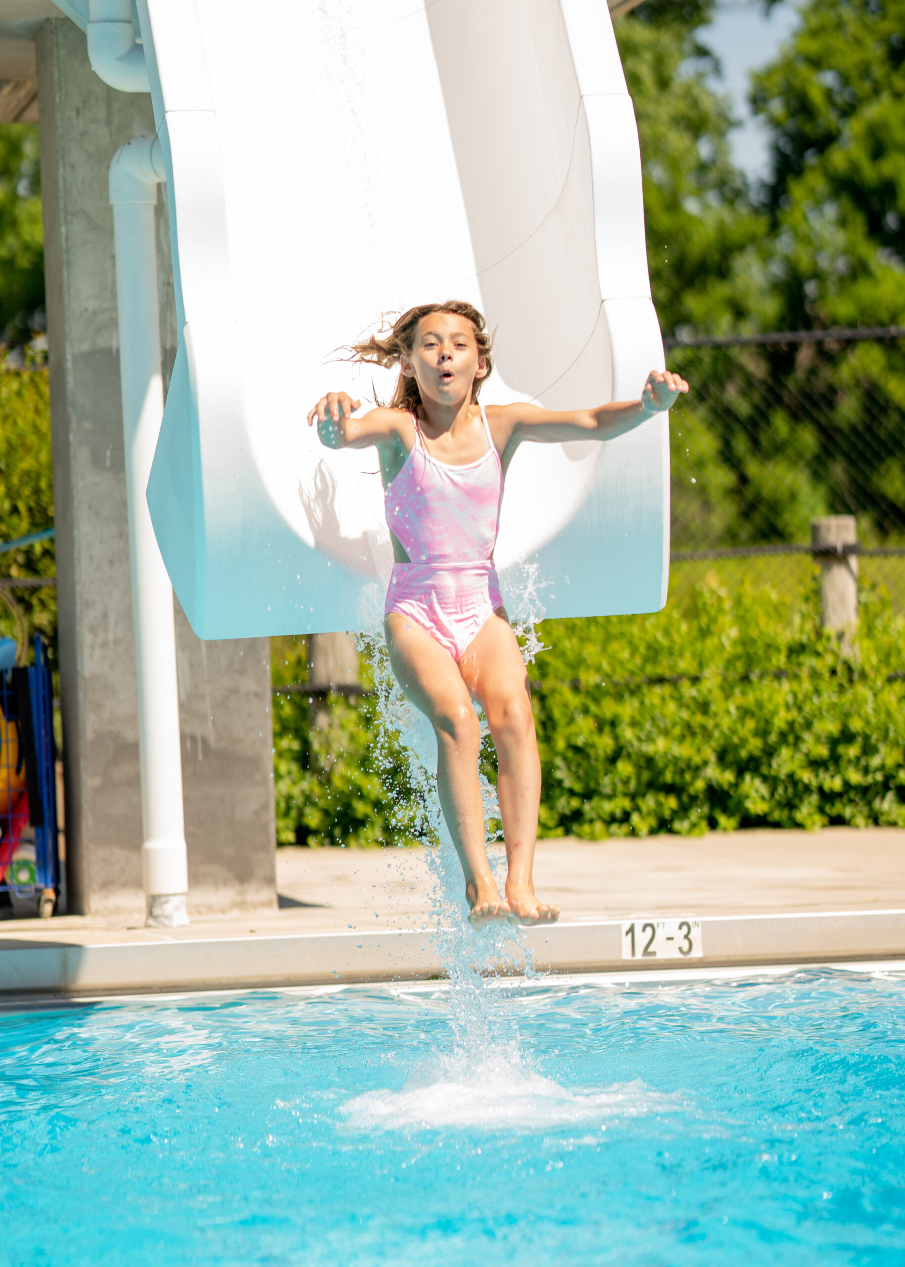 Girl goes off the end of the plunge slide at The Waterpark into the dive pool below, a shocked and excited look on her face.