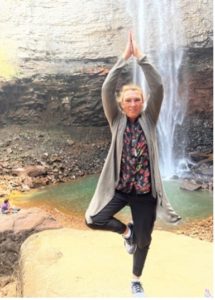 Adaptive instructor Beth does a yoga post in front of a small waterfall outdoors.