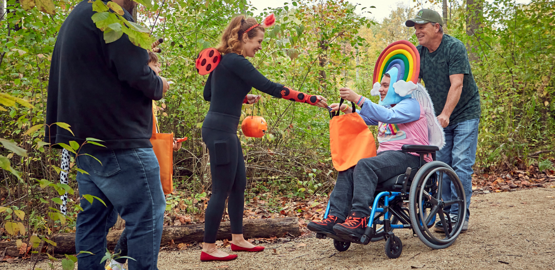 CCPR volunteer hands out candy in a ladybug costume to participant dressed as a rainbow in the clouds at the Sensory Friendly Trick-or-Treat walk.
