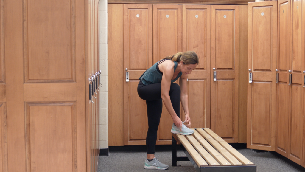 Heather reaches down to tie her shoe in the fitness center locker room.