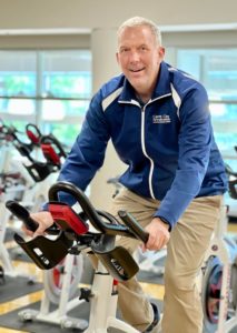 Brian K., MCC Cycle Instructor, sits on a spin class bike in the cycle studio.