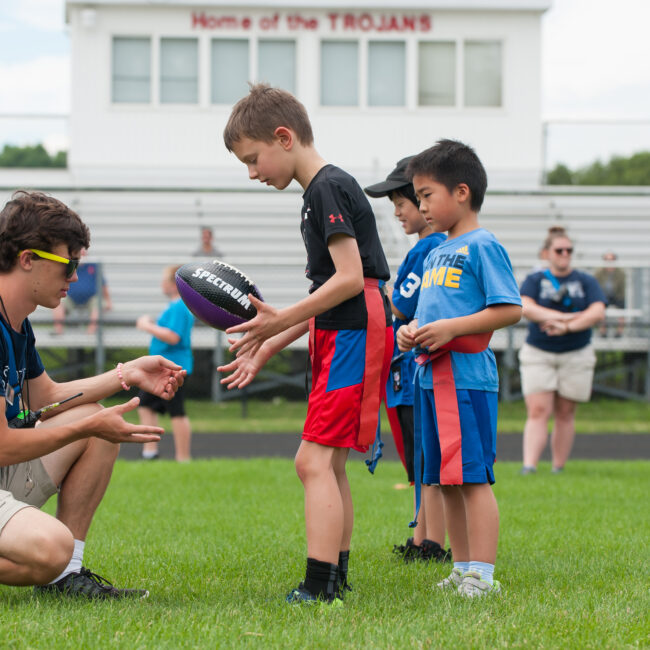 Campers work with instructor to play flag football at Kids at Play summer camp.