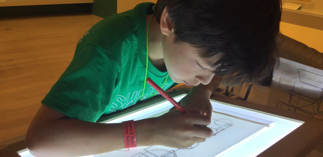 Child traces an art project using a light table during Adventures in Art summer camp.
