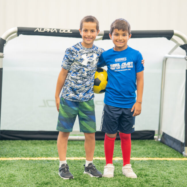 2 campers pose in front of the soccer goal at In the Zone sports camp.