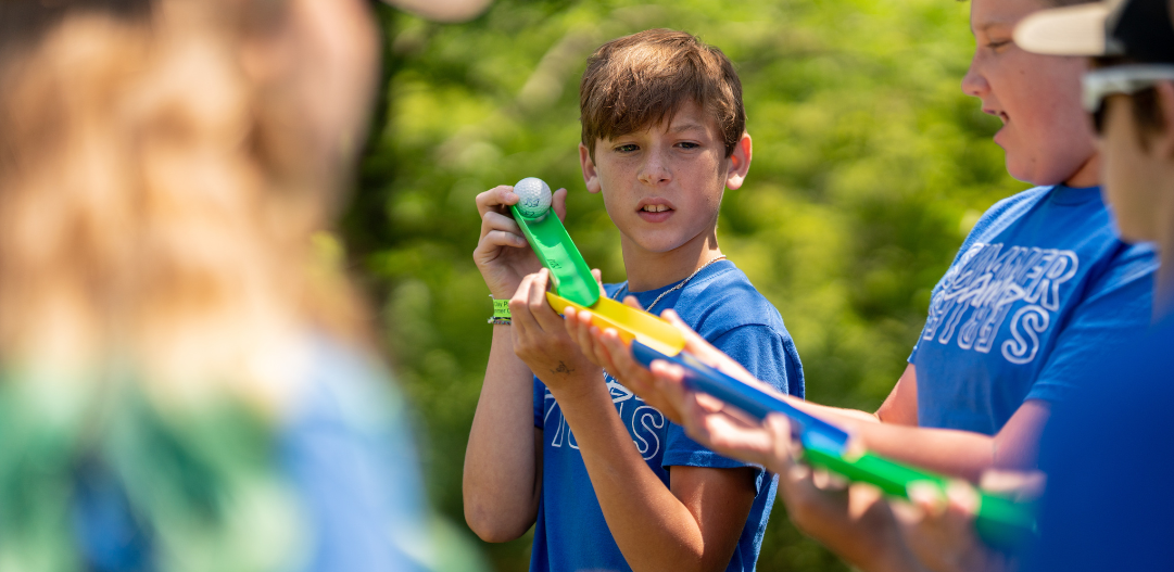 IMPACT participants work together on a team challenge to get their golf ball across the grassy field without dropping it using marble run plastic shoots and pieces.