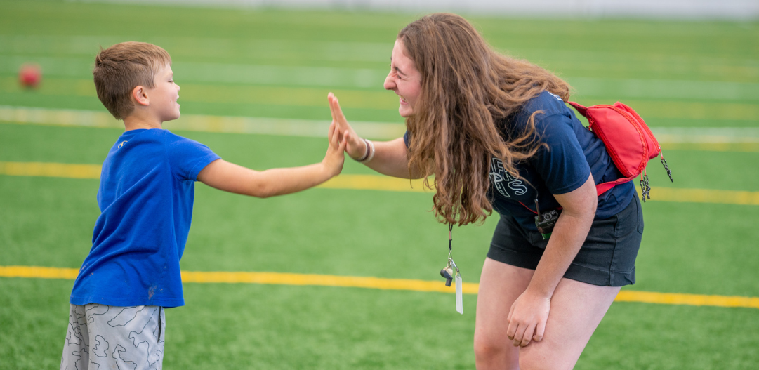 Summer camp counselor high-fives camper.