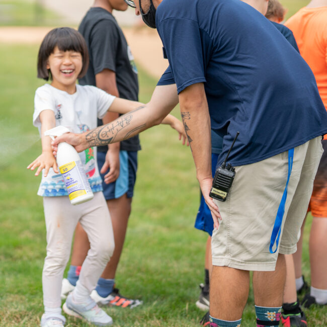 Participants gets sun-sprayed before a game of kickball during camp Kids at Play.