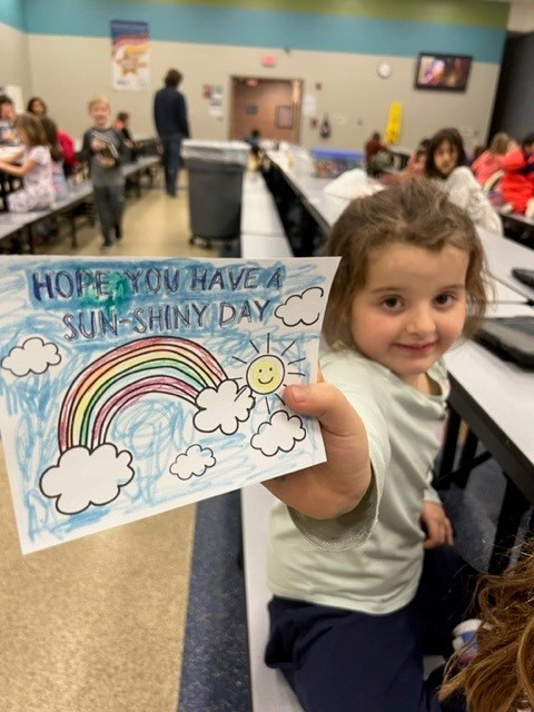 ESE after school program celebrates Random Acts of Kindness Awareness Day. Child holds up a picture wishing you a wonderful day with a rainbow that she colored.