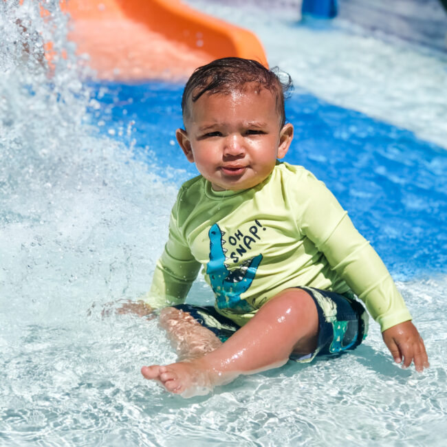 Kiddo enjoying the activity pool at the bottom of the orange slide, where water fountains create an extra splash feature.