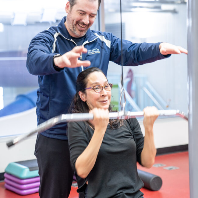 Personal trainer works on weight lifting machine with client.