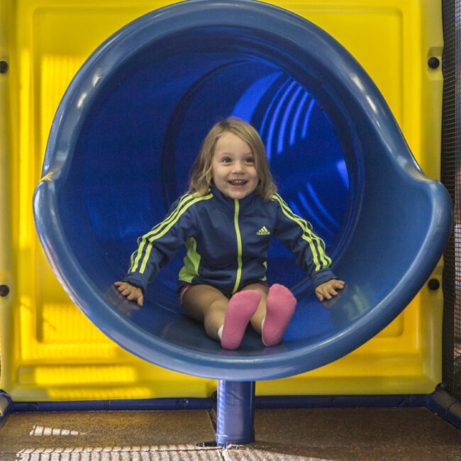 Child smiles at the bottom of the slide in Kidzone at the MCC.