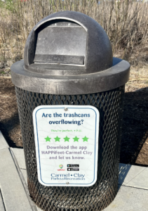Brown trash can on the Monon Greenway with a Happifeet app sign to help people report if the bin is too full.