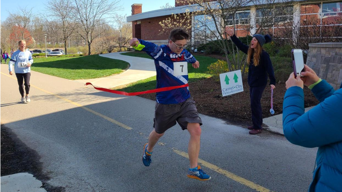 Adaptive 5k race participant charges through the finish line ribbon at the end of the race, victorious!