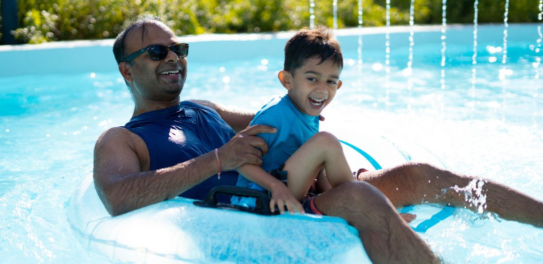 Father and son go under a waterfall feature in the lazy river on an inner-tube at The Waterpark in Carmel.