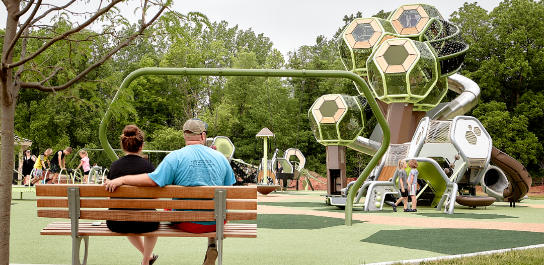 Parents sit on a bench at Meadowlark Park and watch their children play on the playground.