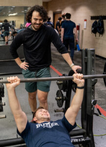 MCC members Sam and Matt workout in the fitness center and spot each other as they use the lifting bench.