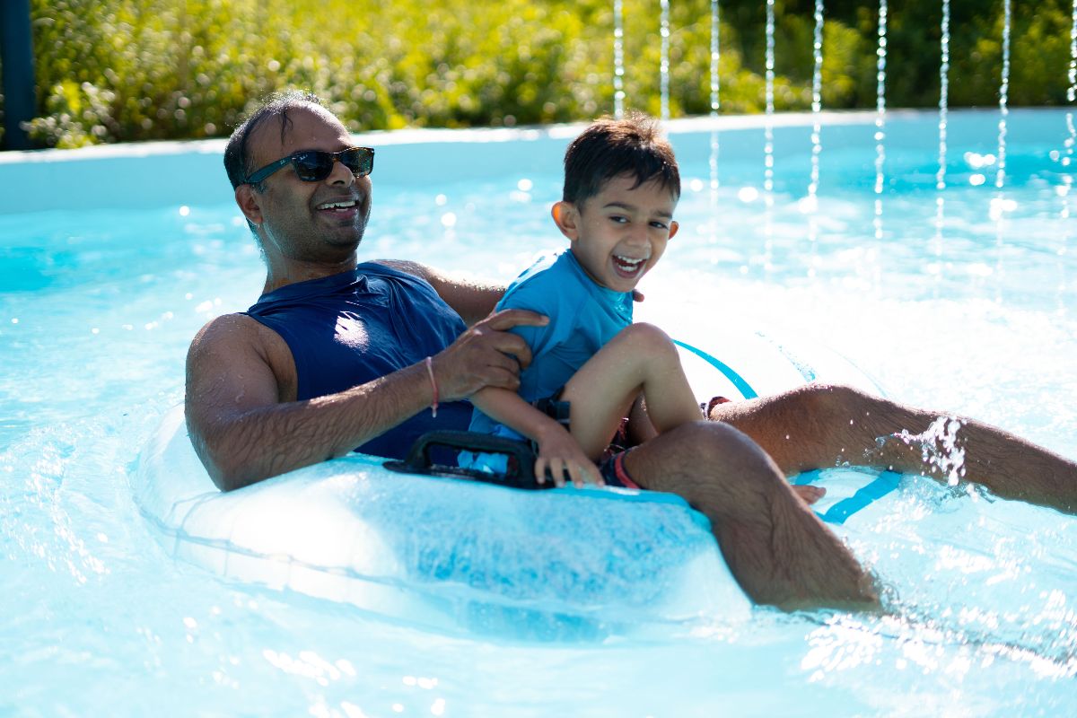 Father and son go under a waterfall feature in the lazy river on an innertube at The Waterpark in Carmel.