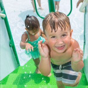 children on green stairs of the kiddie pool having fun and smiling in the splashing water