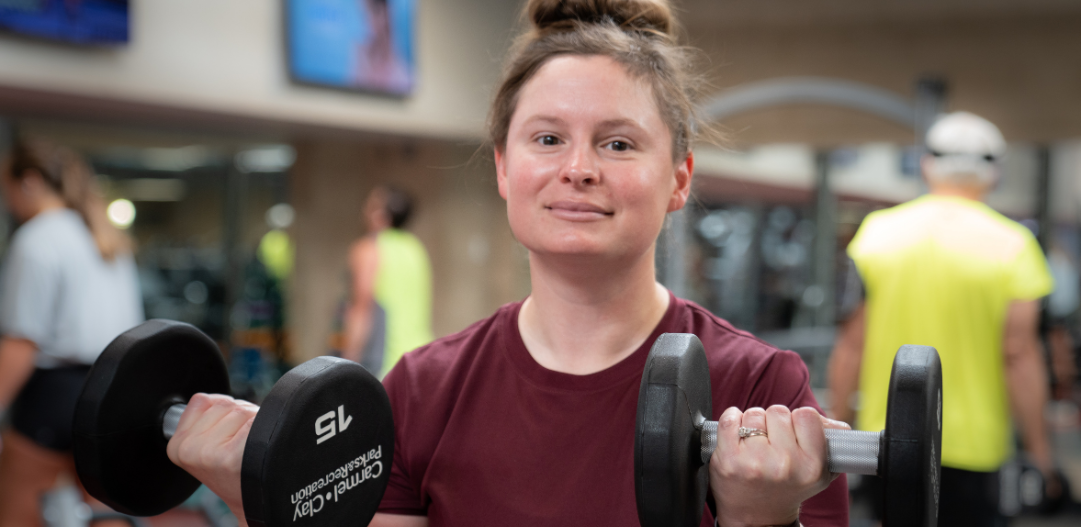 MCC Member Cherish H in fitness center holding up two dumbbells