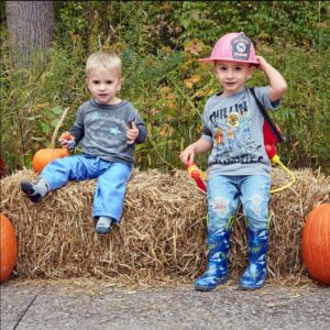 Two kiddos pose on the hay bale with pumpkins along the trails during sensory-friendly trick-or-treat