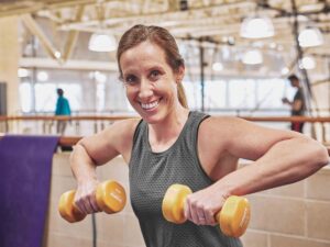 Woman smiles as she lifts weights in Monon Community Center. 